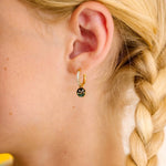 Close-up of an ear wearing a gold earring with a night sky scene made from enamel and clear gemstones, blonde hair in a braid.