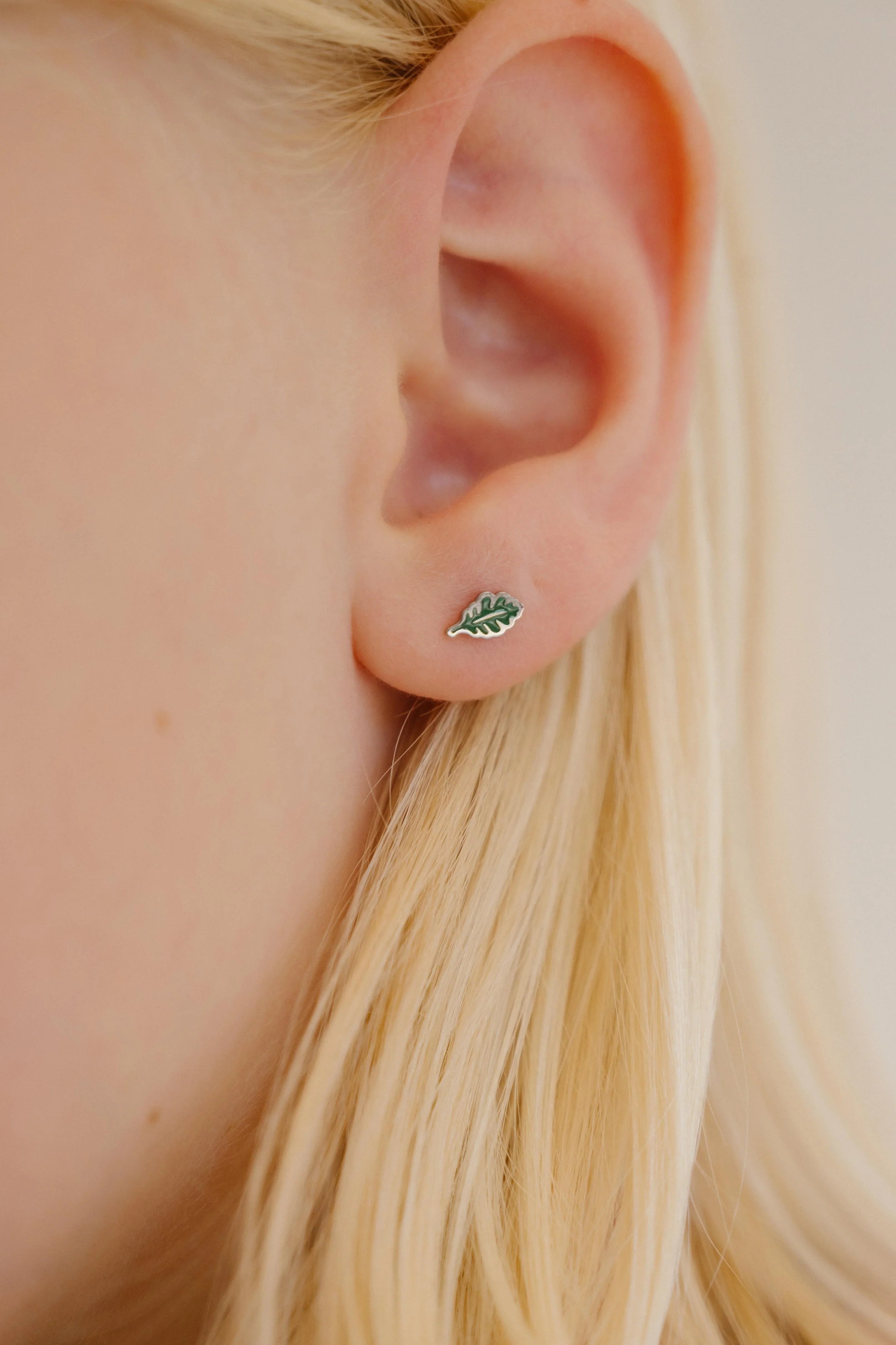 Close-up of a an ear wearing a green oak leaf-shaped enamel stud earring.
