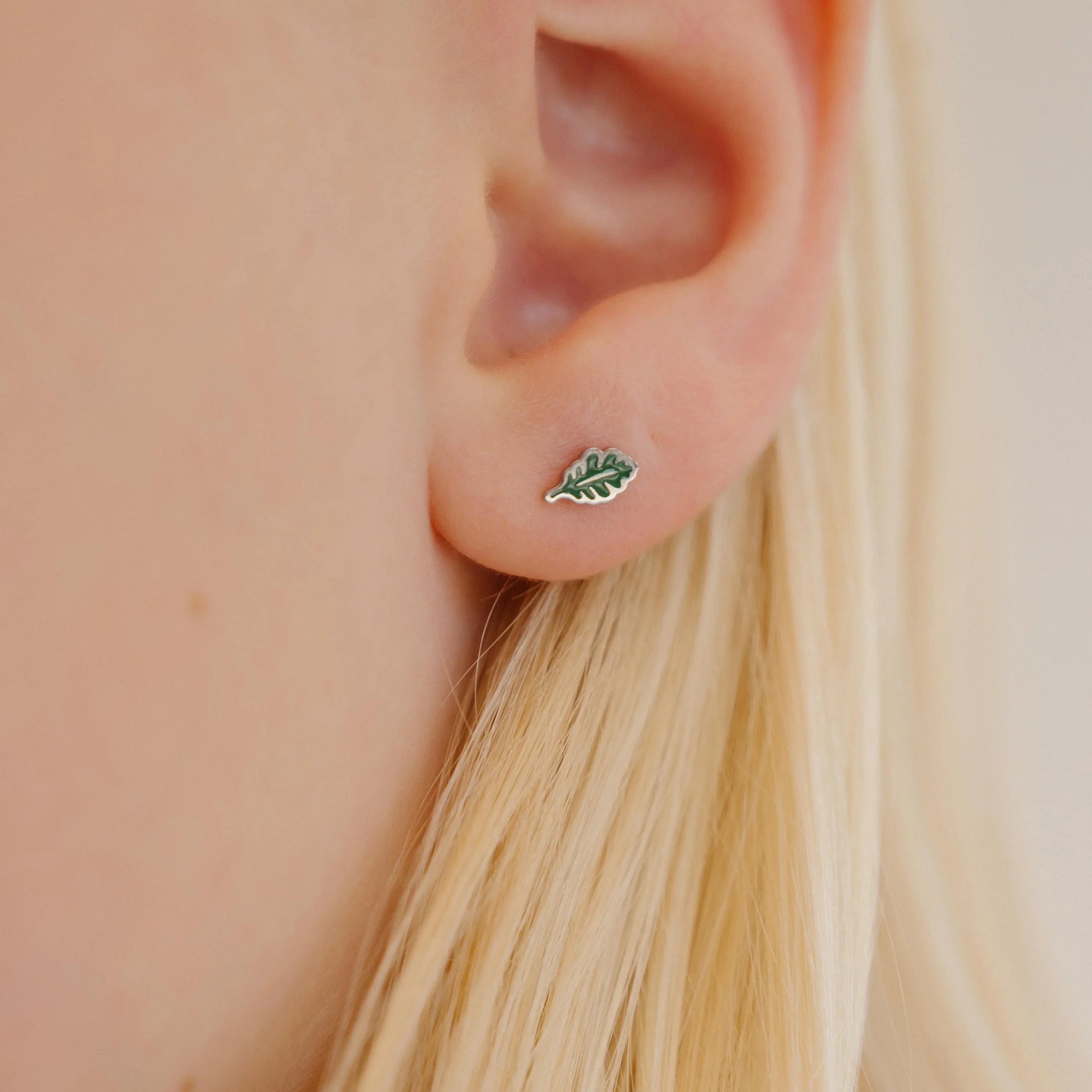 Close-up of a an ear wearing a green oak leaf-shaped enamel stud earring.