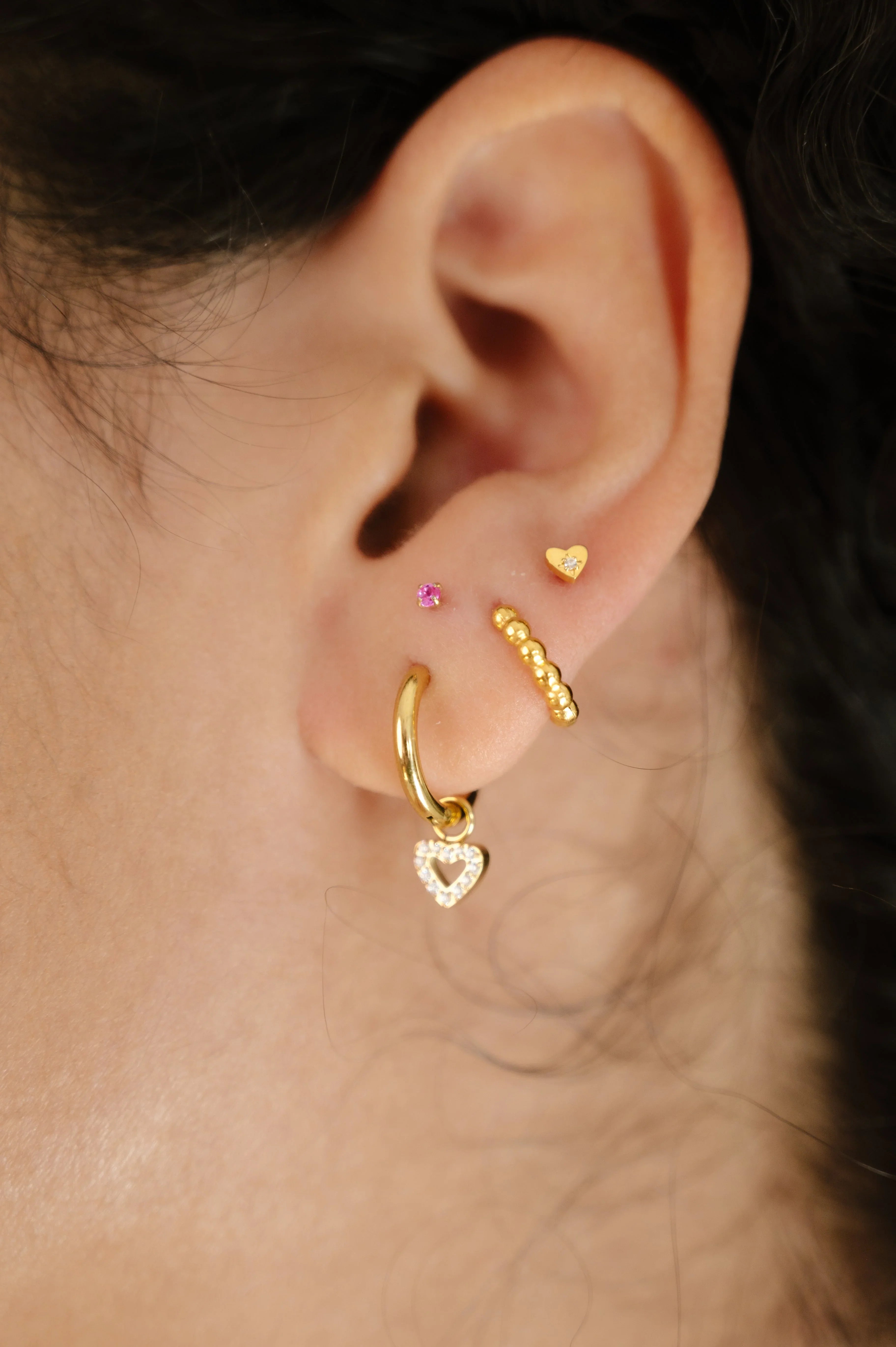 Close-up of an ear with gold hoop earrings on a neutral background