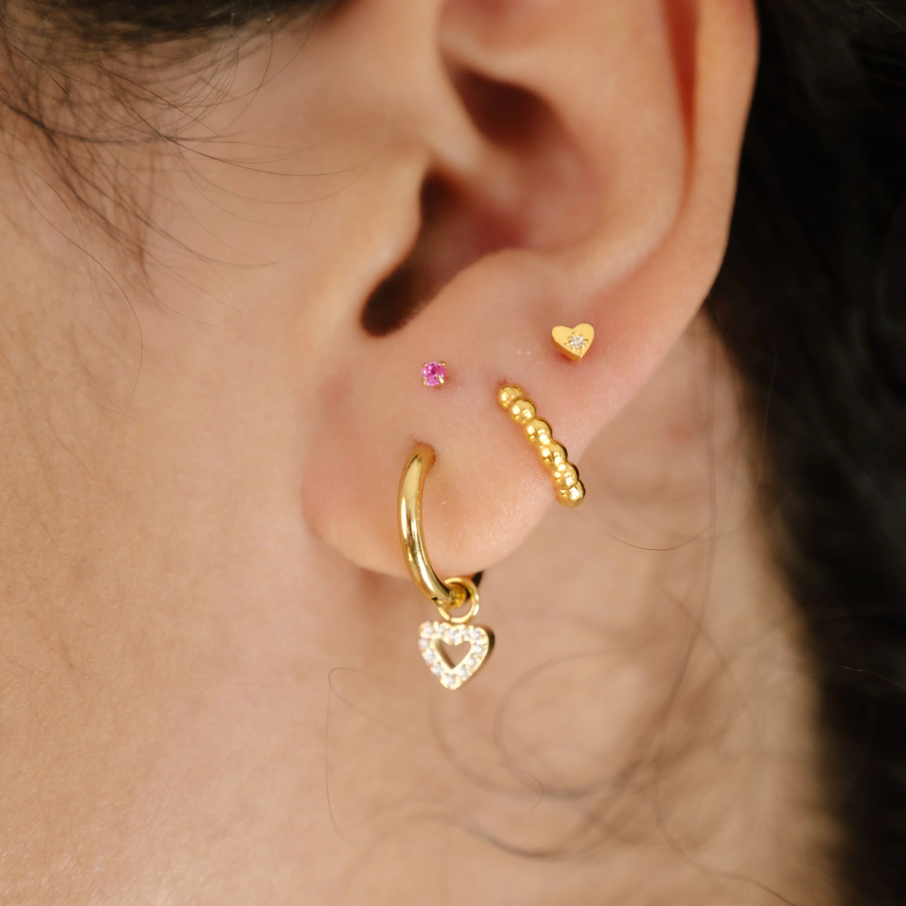 Close-up of an ear with gold hoop earrings on a neutral background