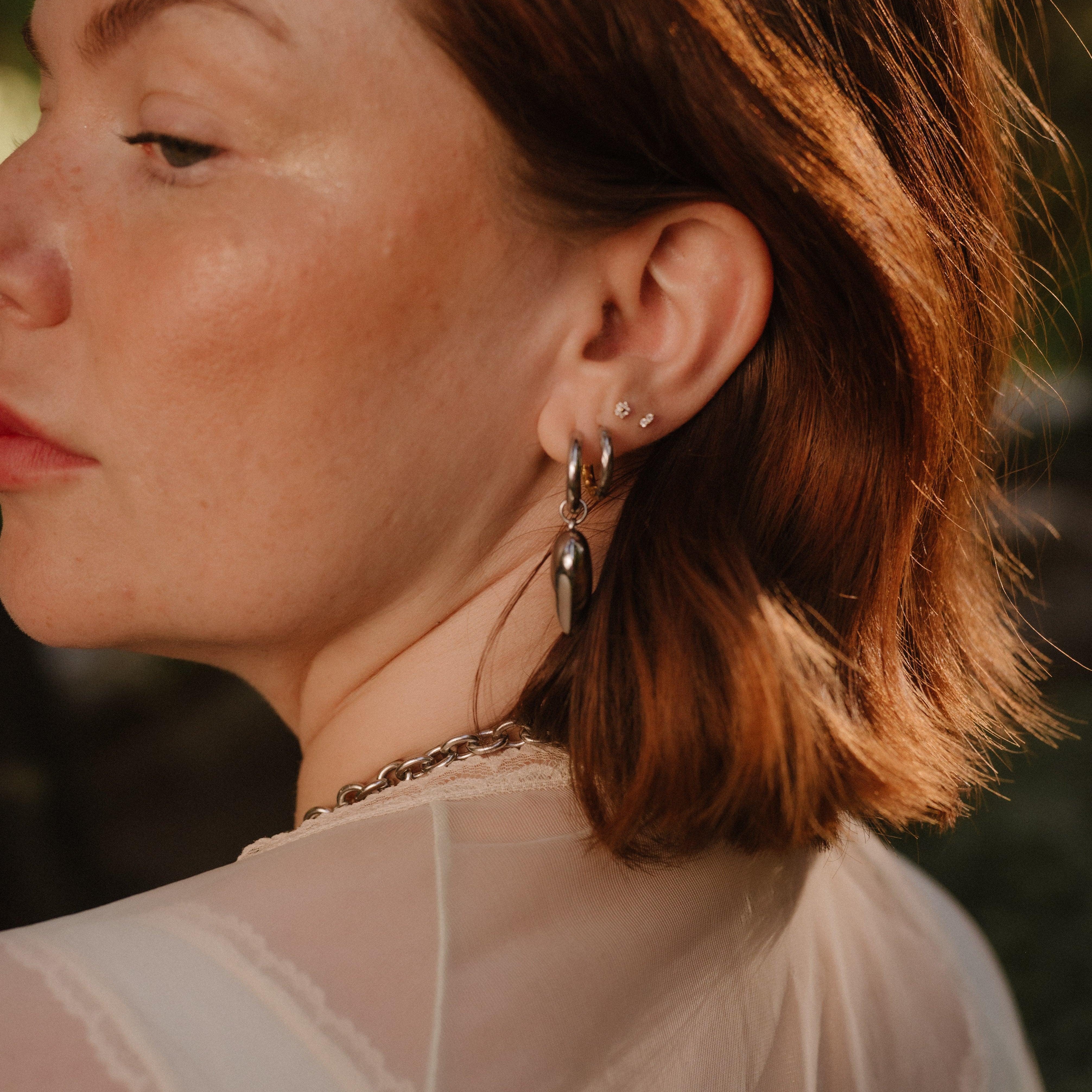 Close-up of a person wearing earrings with a blurred natural background