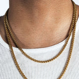 A close-up of a person's neck and upper chest wearing a double-layered gold chain necklace over a white ribbed tank top.