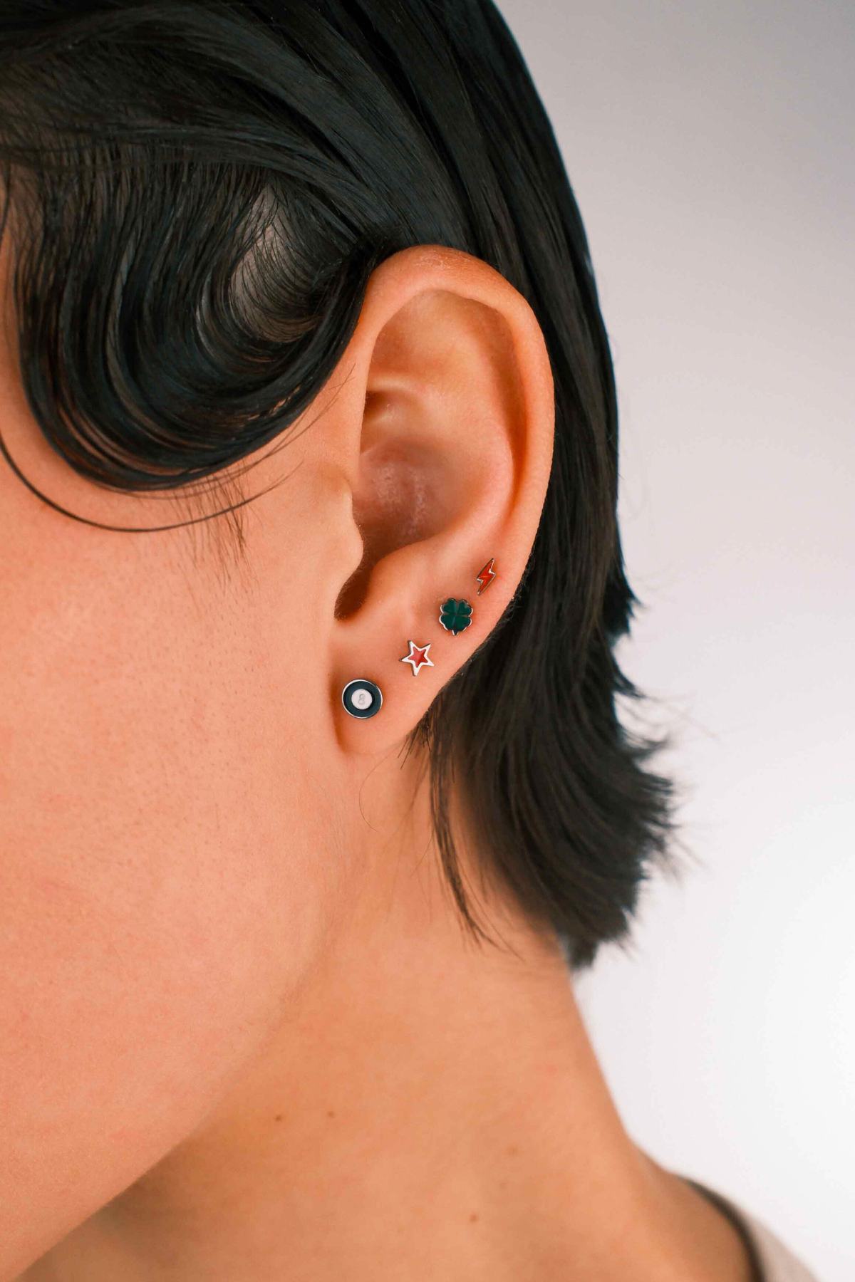 Photo of a person wearing multiple flat back stud earrings, including 1 in the shape of an 8 ball in black and white