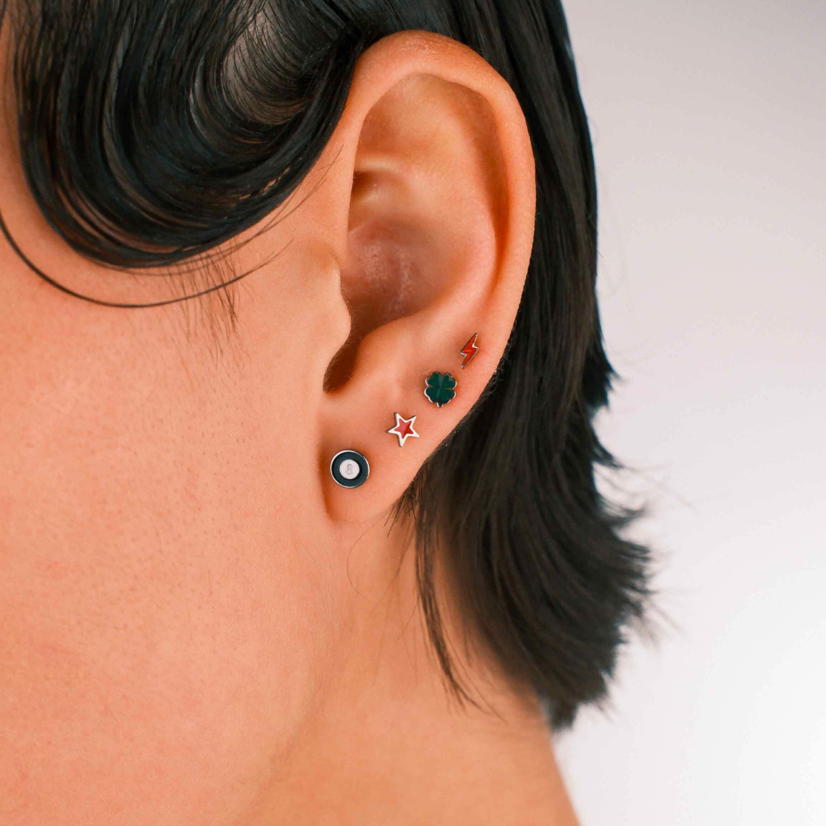 Photo of a person wearing multiple flat back stud earrings, including 1 in the shape of an 8 ball in black and white