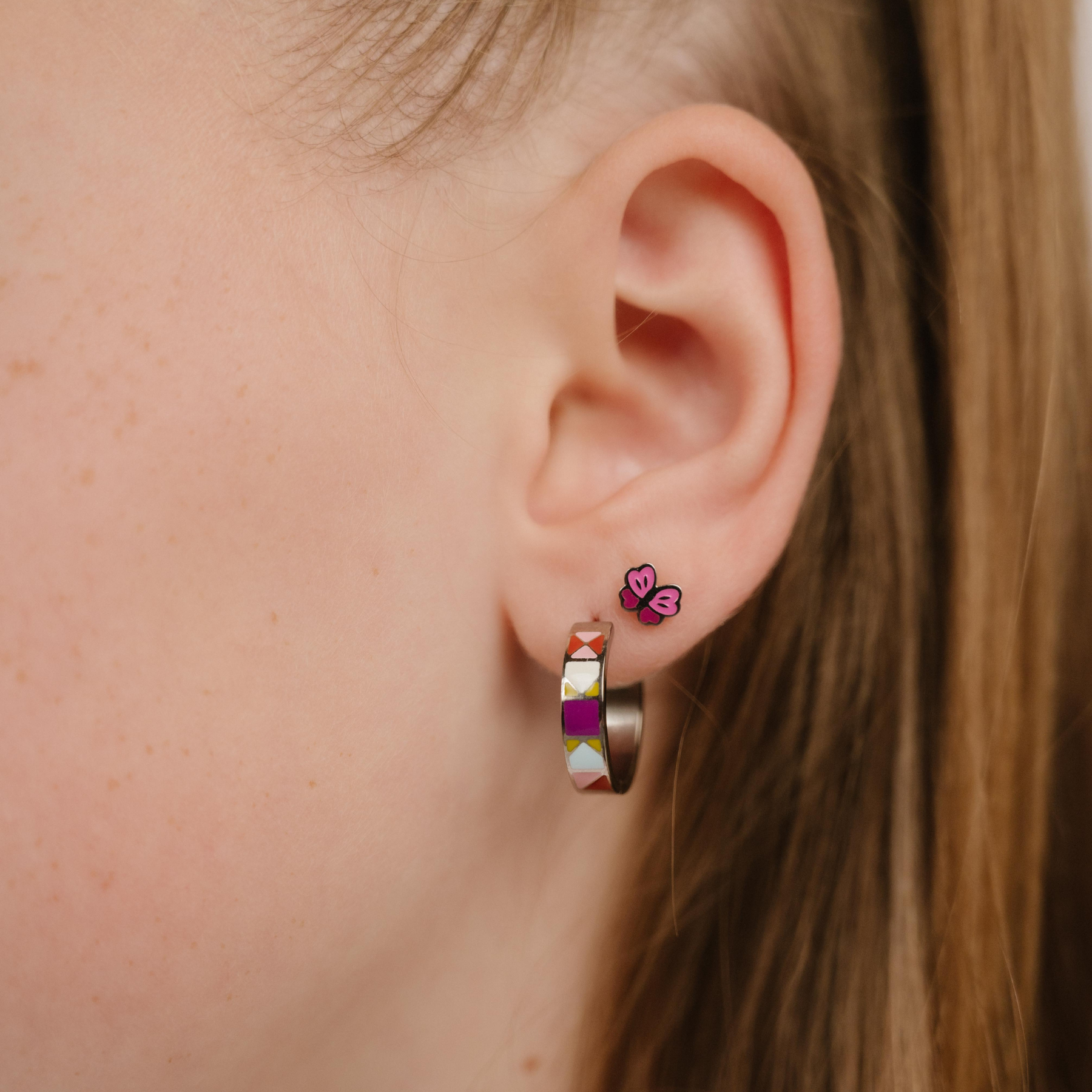 A close up of a butterfly shaped flat back stud earring with wings of pink enamel and titanium metal.
