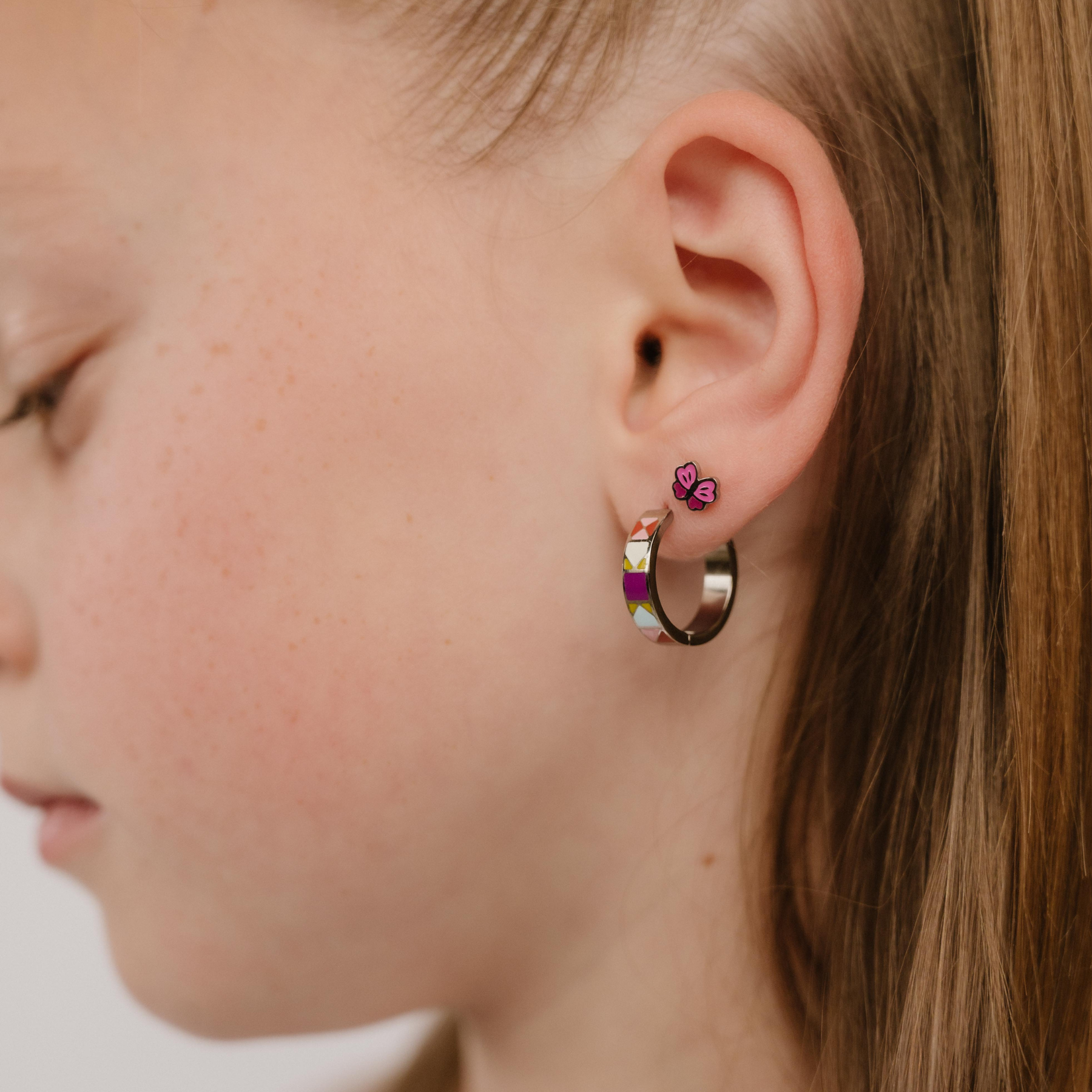 A model wearing butterfly shaped flat back stud earring with wings of pink enamel and titanium metal.