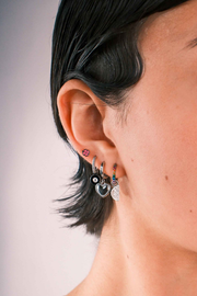 Close-up of a person wearing multiple silver earrings including a clover shaped flat back stud in pink enamel. 