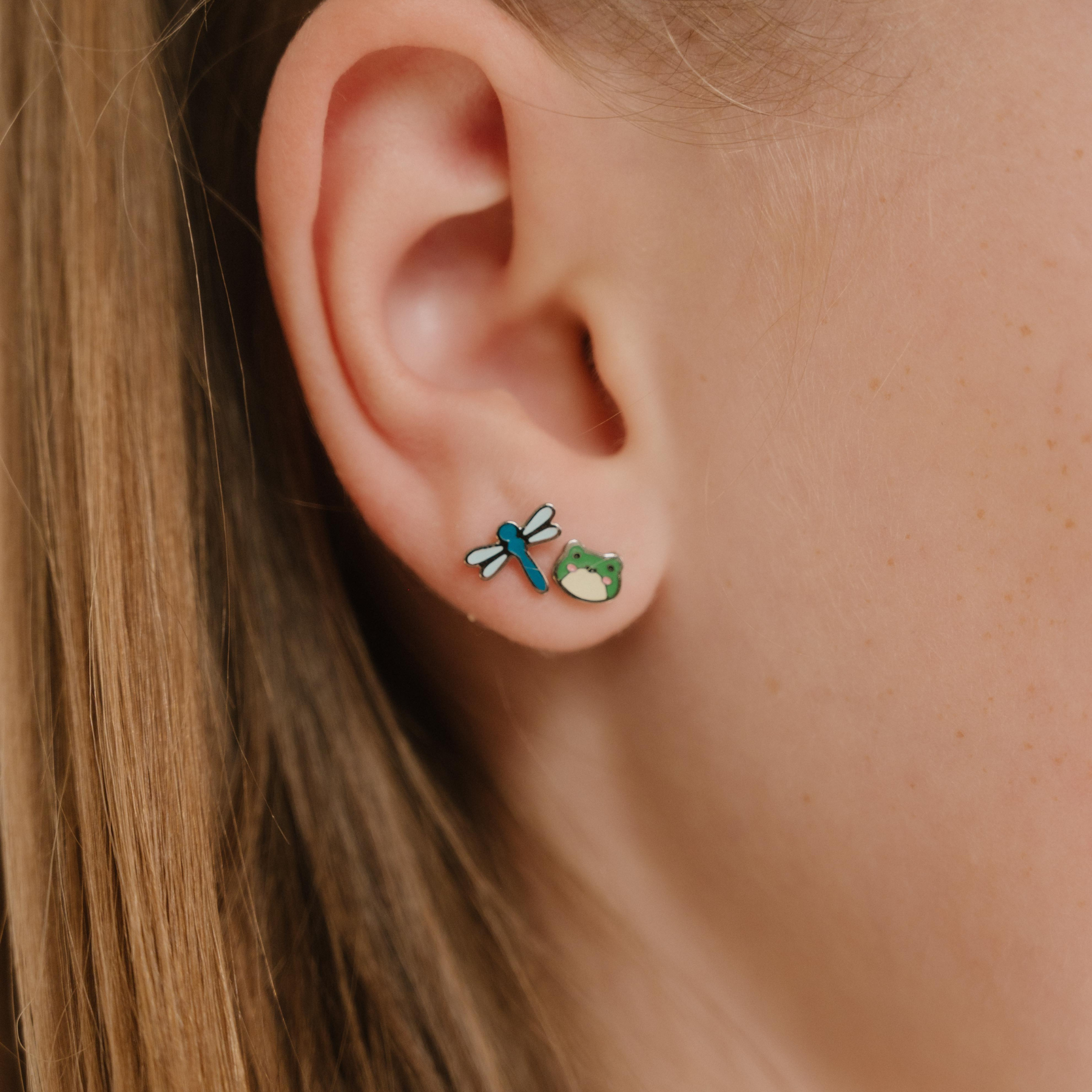 A close up of a dragonfly shaped flat back stud earring with blue enamel and titanium metal.