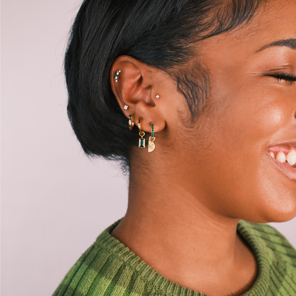 Close-up of a person wearing multiple earrings with a plain background