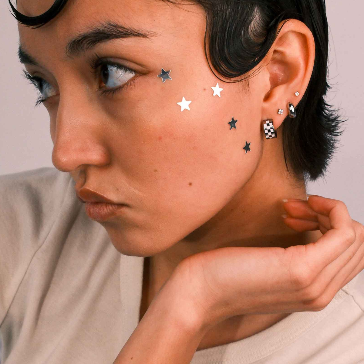 Close-up of a person wearing multiple earrings against a neutral background