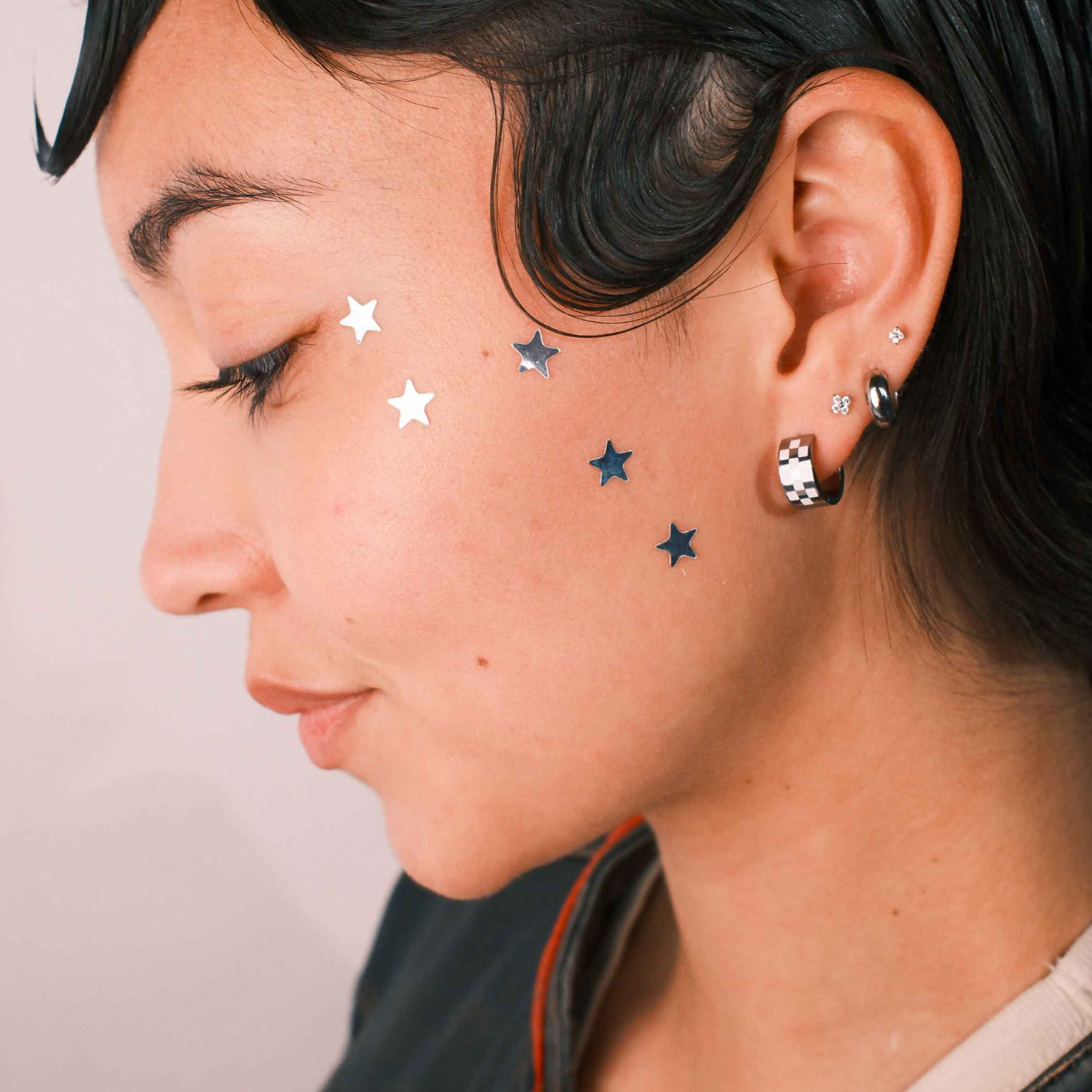 Close-up of a person wearing multiple earrings against a neutral background
