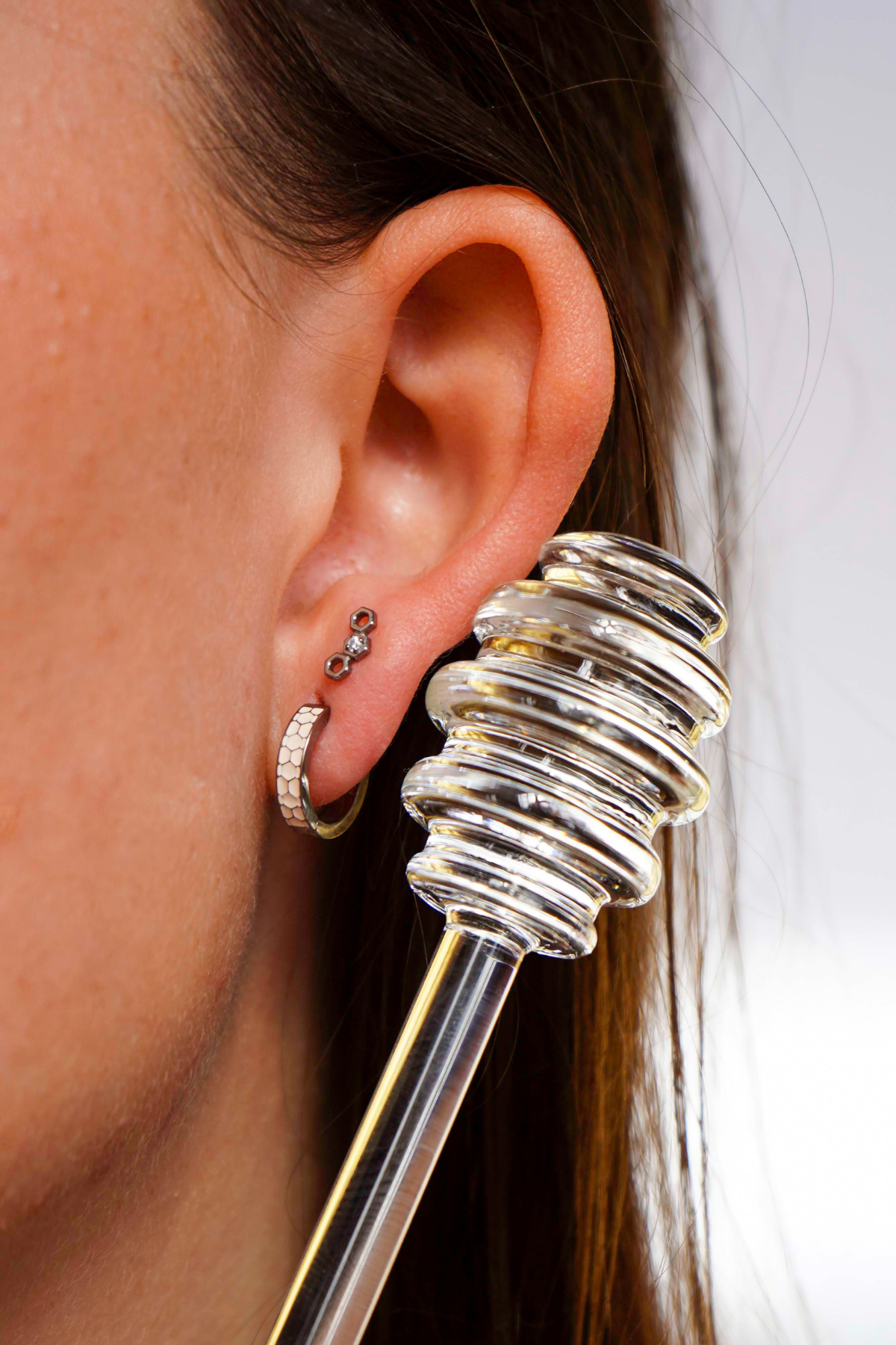 Close up of a model wearing a hexagon shaped flat back stud earring made from ASTM F136 implant-grade titanium, with a clear zirconia stone, against a blurred  background. 