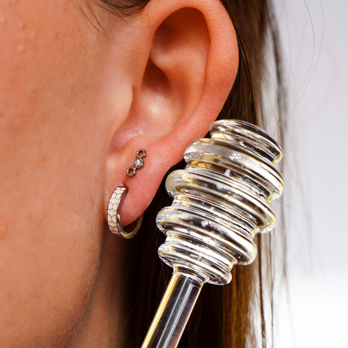 Close up of a model wearing a hexagon shaped flat back stud earring made from ASTM F136 implant-grade titanium, with a clear zirconia stone, against a blurred  background. 
