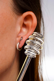Close up of a model wearing a hexagon shaped flat back stud earring made from ASTM F136 implant-grade titanium, with a clear zirconia stone, against a blurred  background. 