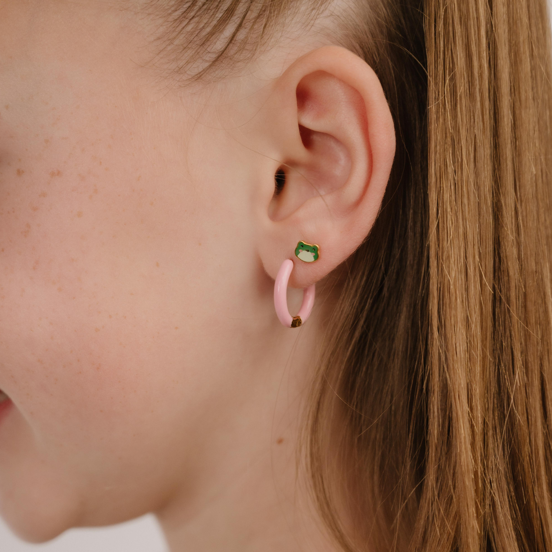 A close up of a frog shaped flat back stud with green enamel and gold-plated titanium metal.