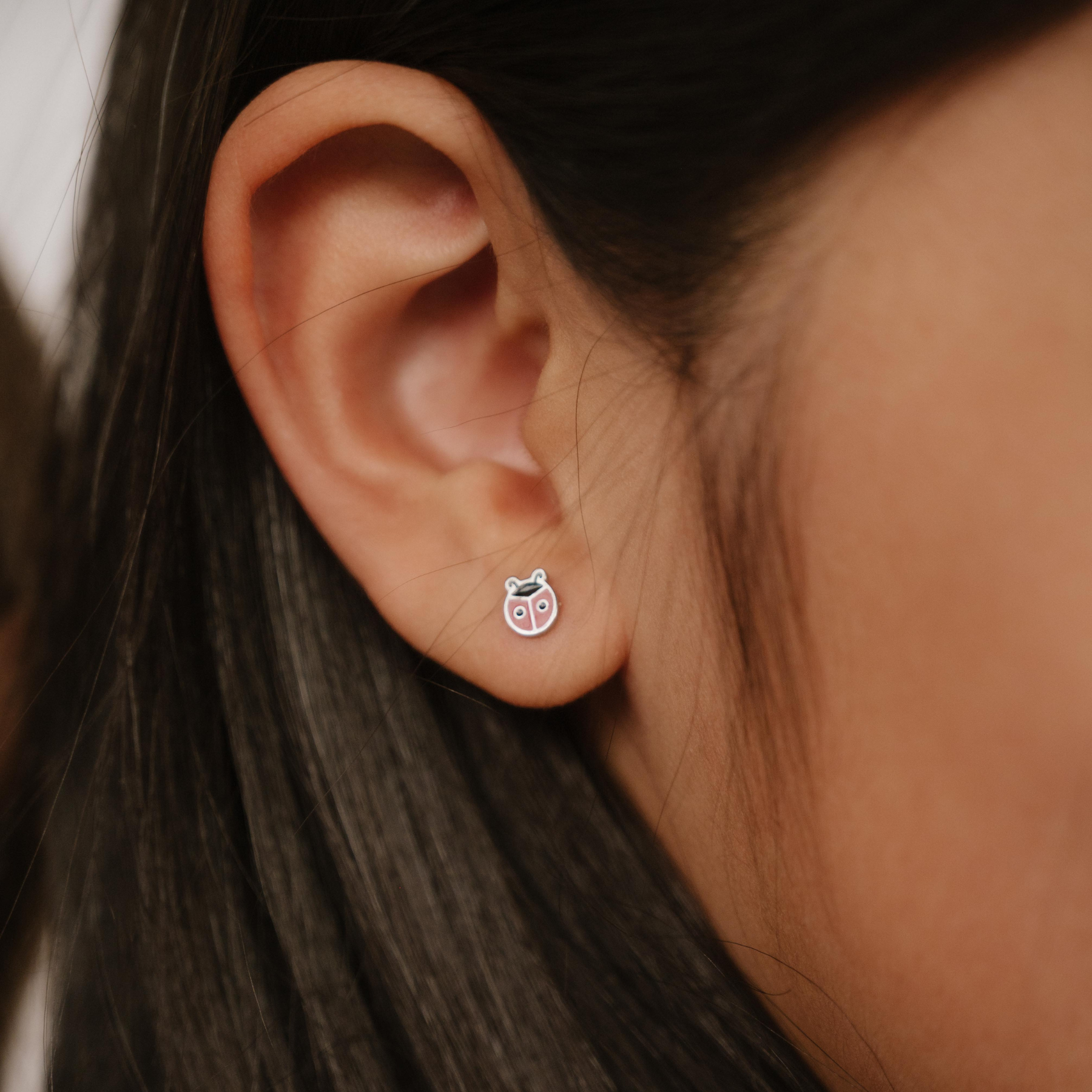 A close up of a ladybug shaped flat back stud with red enamel and titanium metal.