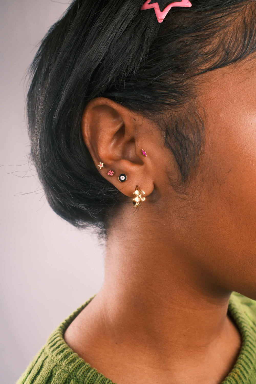 Close-up of an ear with multiple earrings, including a lightning bolt flat back stud in hot pink enamel. 