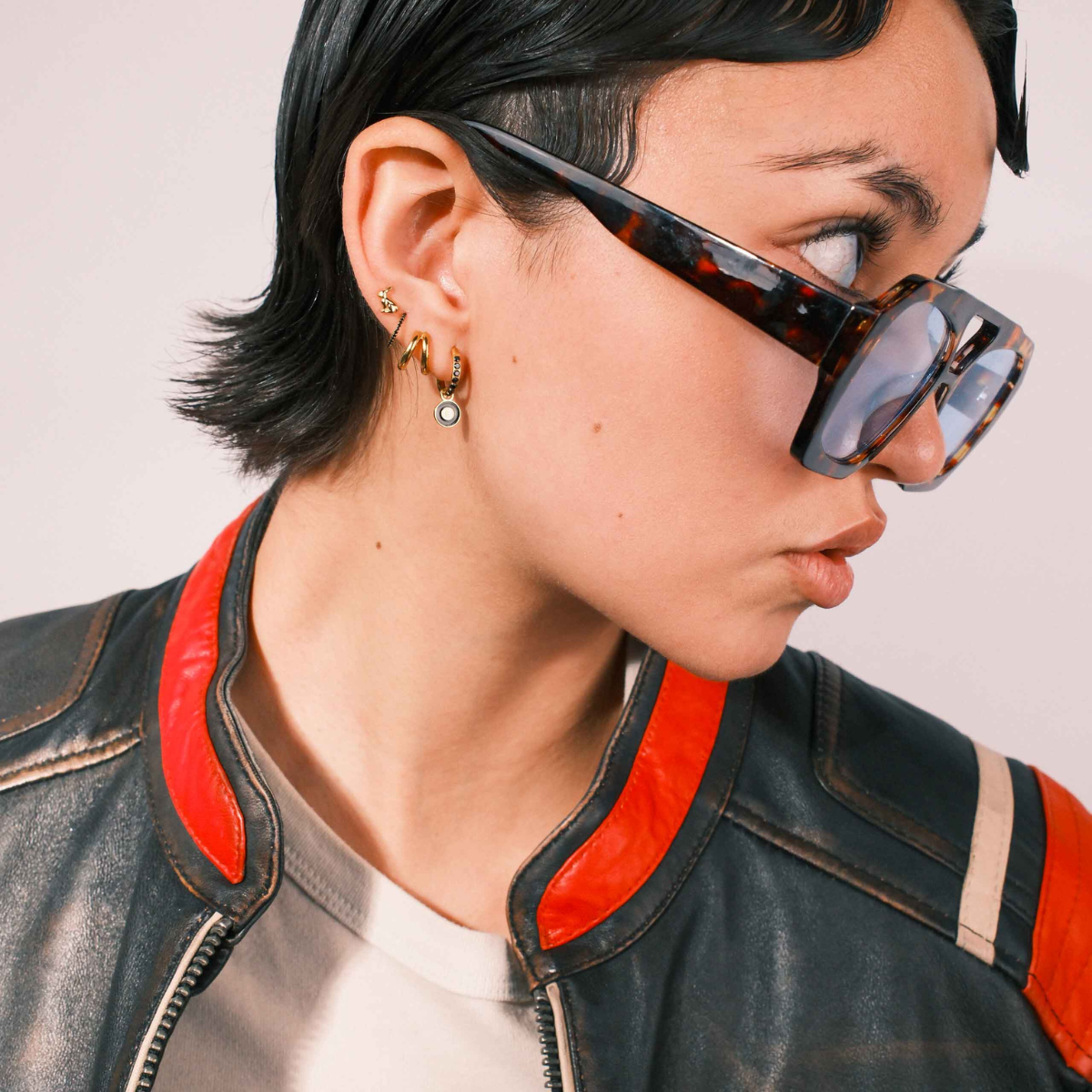 Close-up of an ear wearing gold and black earrings with a plain background