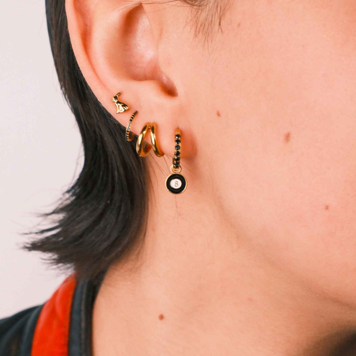 Close-up of an ear wearing gold and black earrings with a plain background
