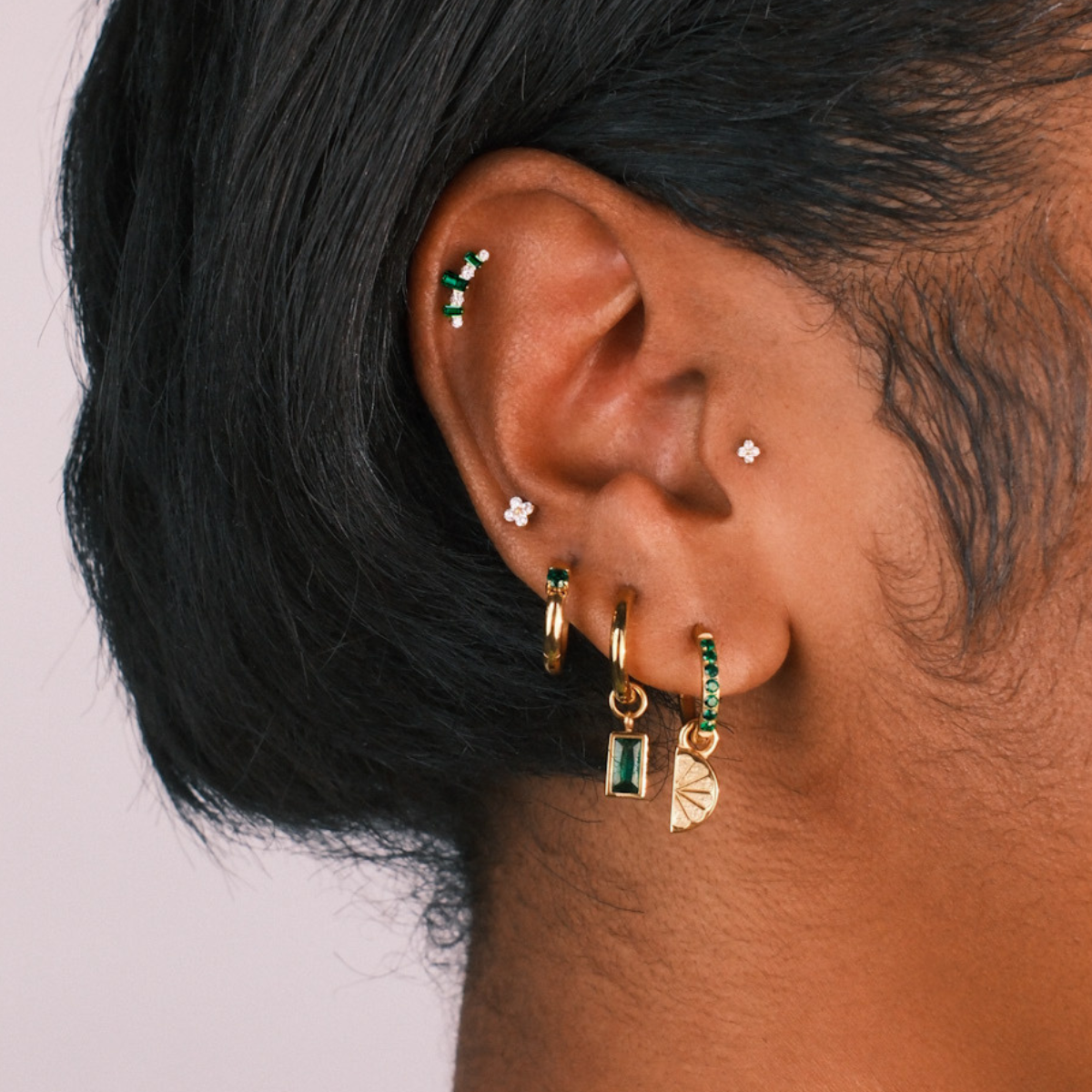 Close-up of an ear with multiple earrings on a plain background
