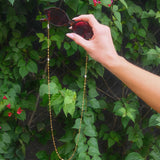 Hand holding sunglasses with a chain against a green leafy background