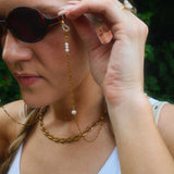 Woman wearing sunglasses with a long gold chain.