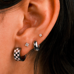 Close-up of an ear with multiple earrings including a checkered pattern earring.