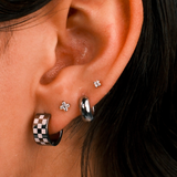 Close-up of an ear with multiple earrings including a checkered pattern earring.