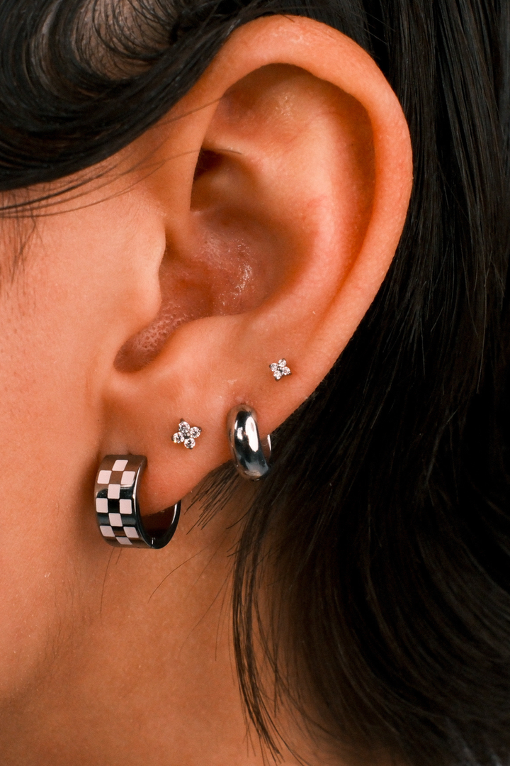 Close-up of an ear with multiple earrings including a checkered pattern earring.