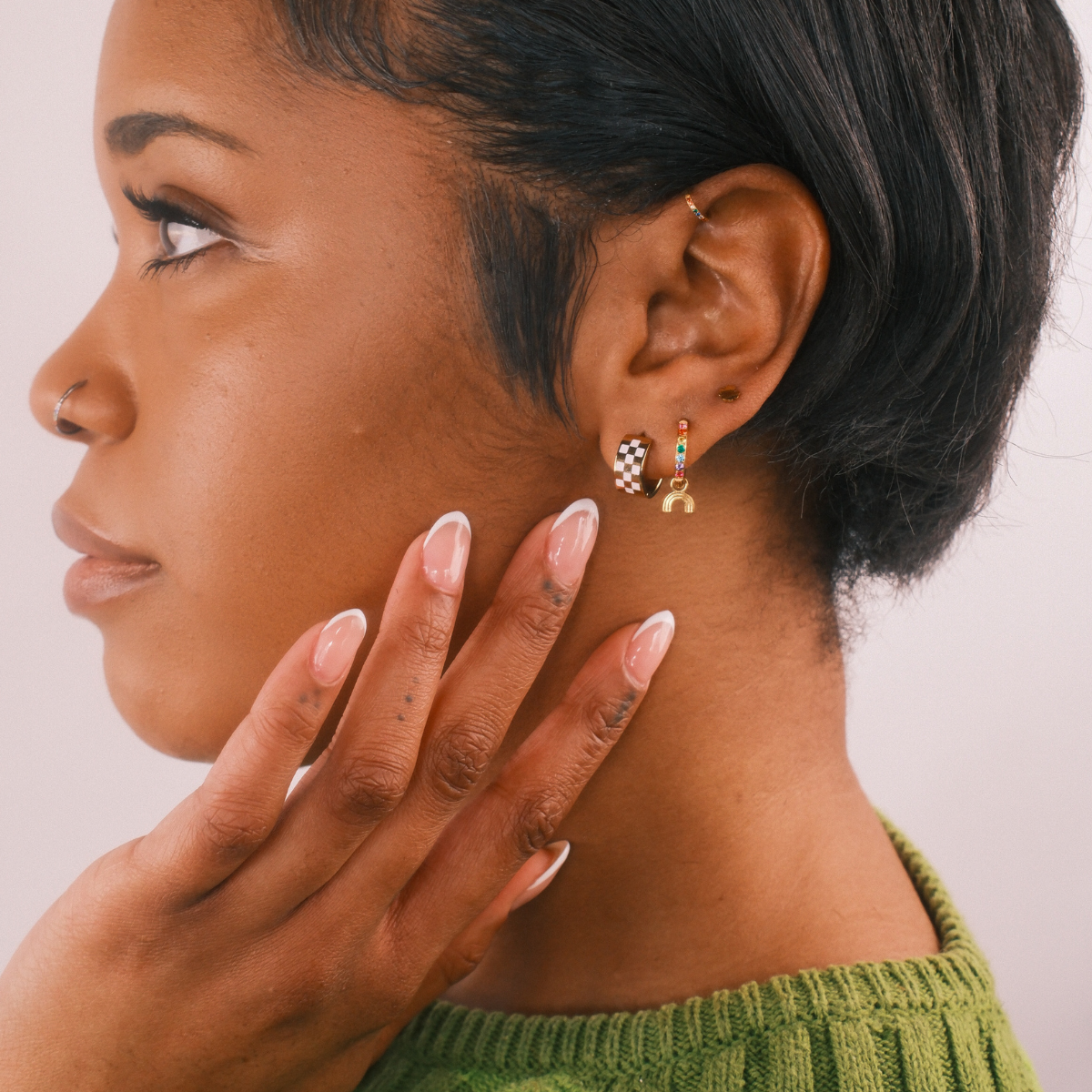Woman with short black hair wearing colorful star-shaped hair clips, green sweater, and gold earrings.