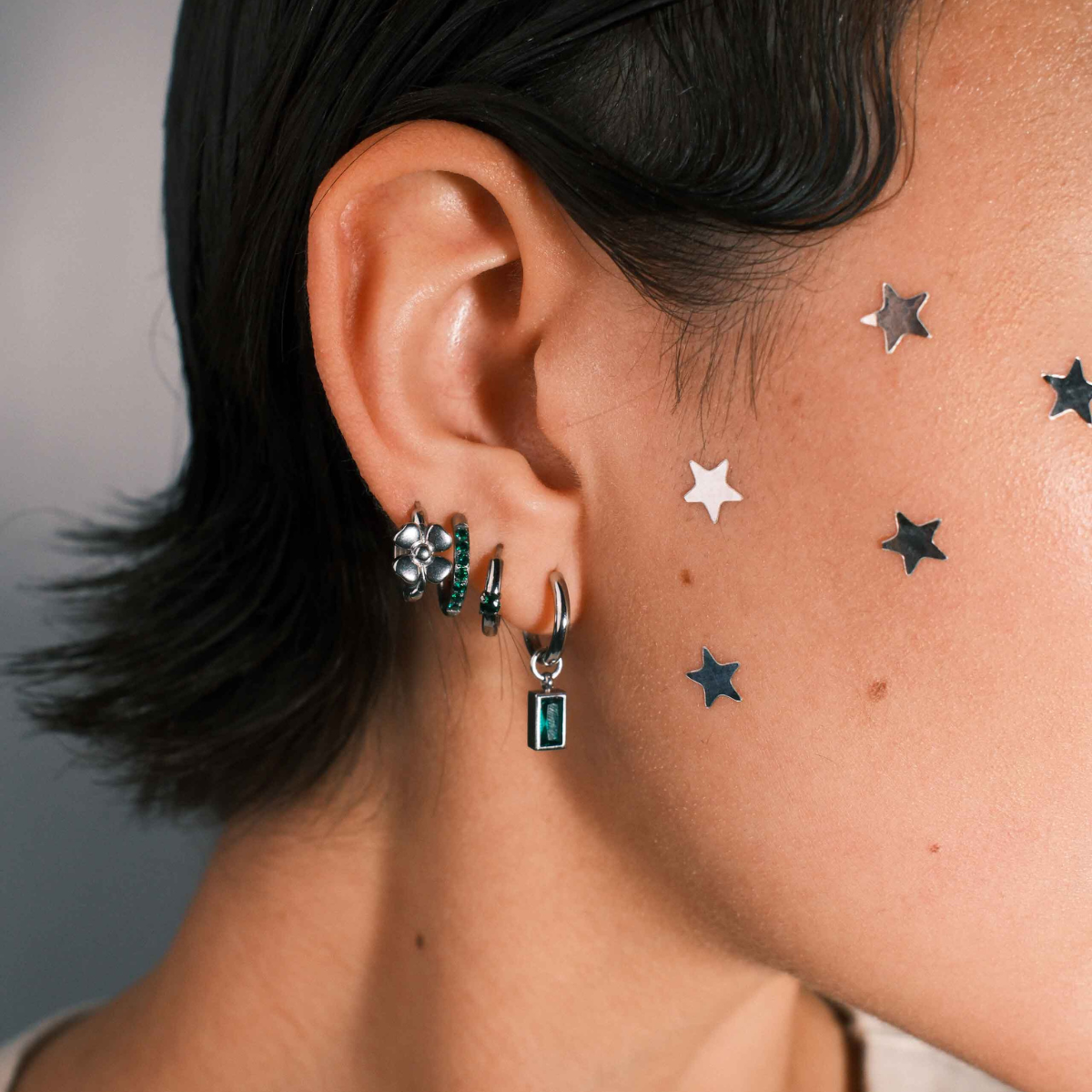 Close up of a person wearing multiple silver hoop earrings against a neutral background