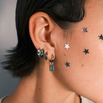 Close up of a person wearing multiple silver hoop earrings against a neutral background