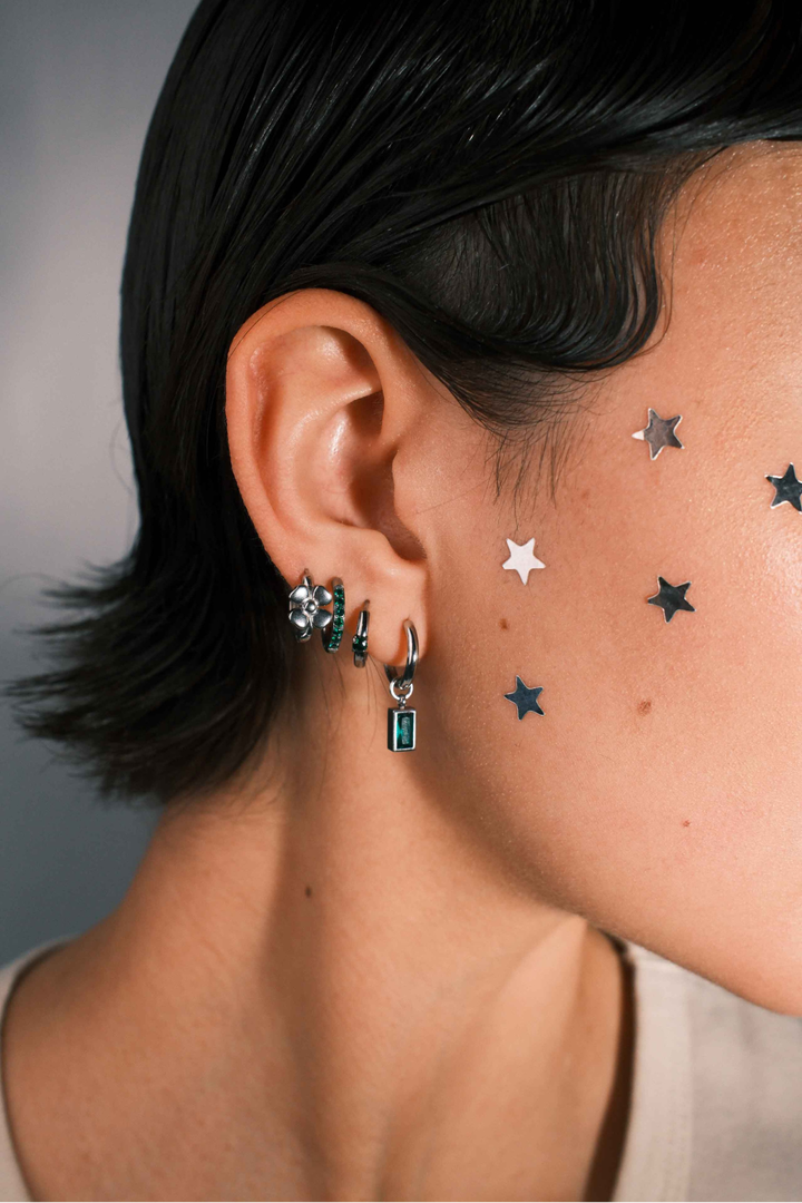 Close up of a person wearing multiple silver hoop earrings against a neutral background