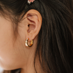 A close up of a model wearing a hoop earring made from 18K gold-plated titanium metal, with a line enamel daisy in white and yellow decorating the hoop.