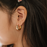 A close up of a model wearing a hoop earring made from 18K gold-plated titanium metal, with a line enamel daisy in white and yellow decorating the hoop.