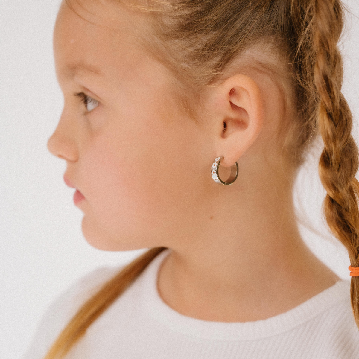 Profile of a girl with silver hoop earrings braided hair wearing a white shirt on a plain background