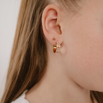 A close up of a model wearing a hoop earring made from gold-plated titanium metal, with folk-art style floral patterns in pink, dark pink, and white enamel.