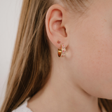 A close up of a model wearing a hoop earring made from gold-plated titanium metal, with folk-art style floral patterns in pink, dark pink, and white enamel.