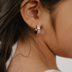A close up of a model wearing a hoop earring made from titanium metal, with folk-art style floral patterns in pink, dark pink, and white enamel.