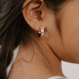 A close up of a model wearing a hoop earring made from titanium metal, with folk-art style floral patterns in pink, dark pink, and white enamel.