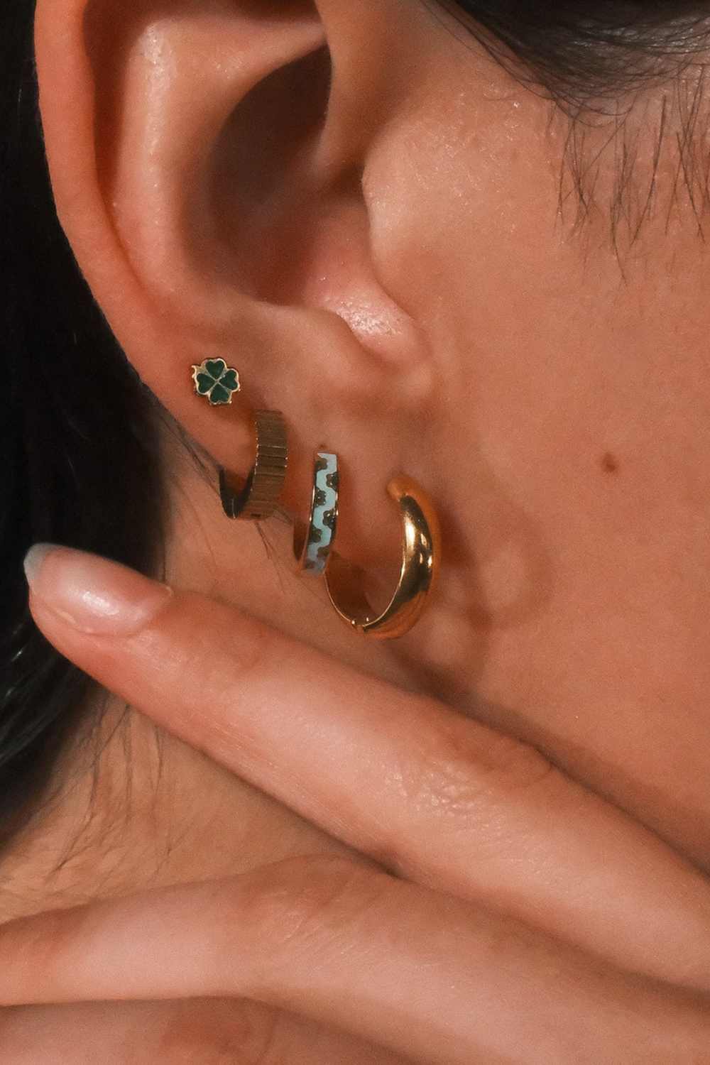 Close-up of an ear with multiple earrings on a neutral background