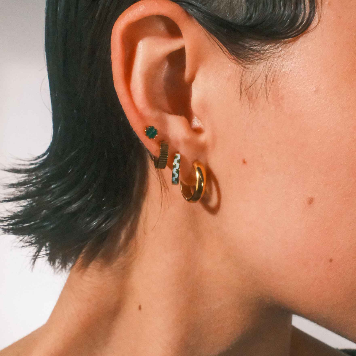 Close-up of an ear with multiple earrings against a neutral background