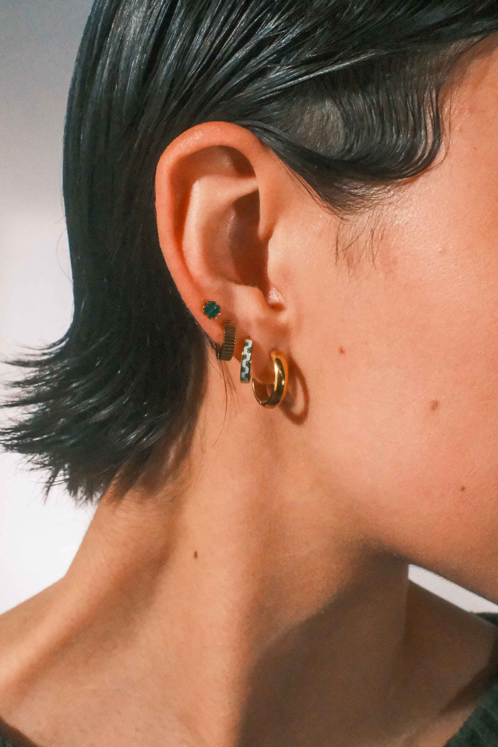 Close-up of an ear with multiple earrings against a neutral background