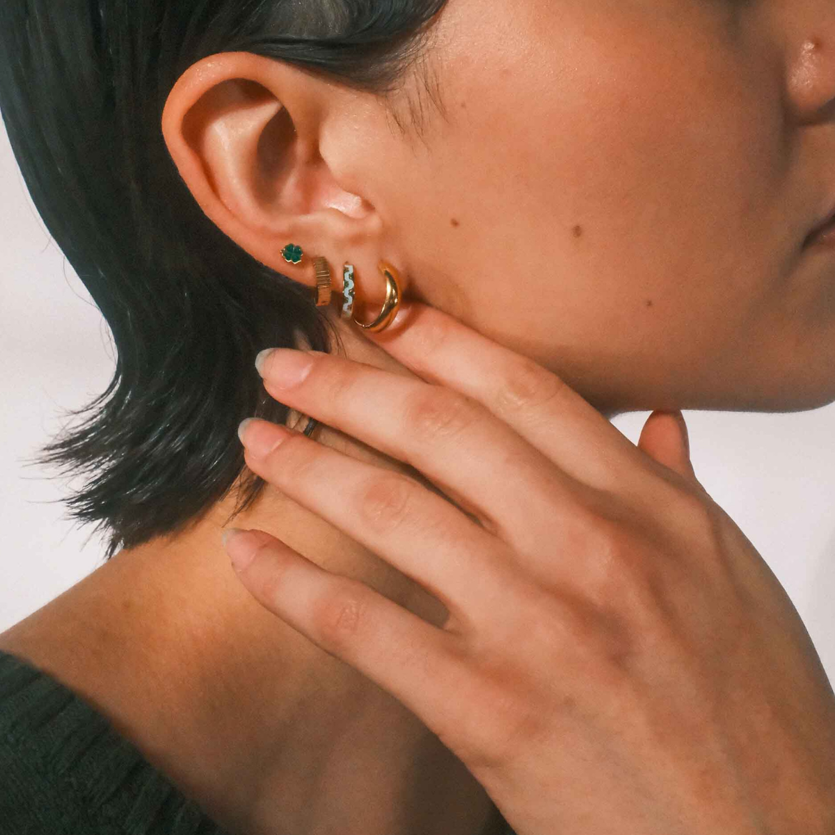 Close-up of a person wearing multiple gold earrings with a neutral background