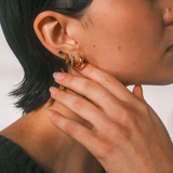 Close-up of a person wearing multiple gold earrings with a neutral background