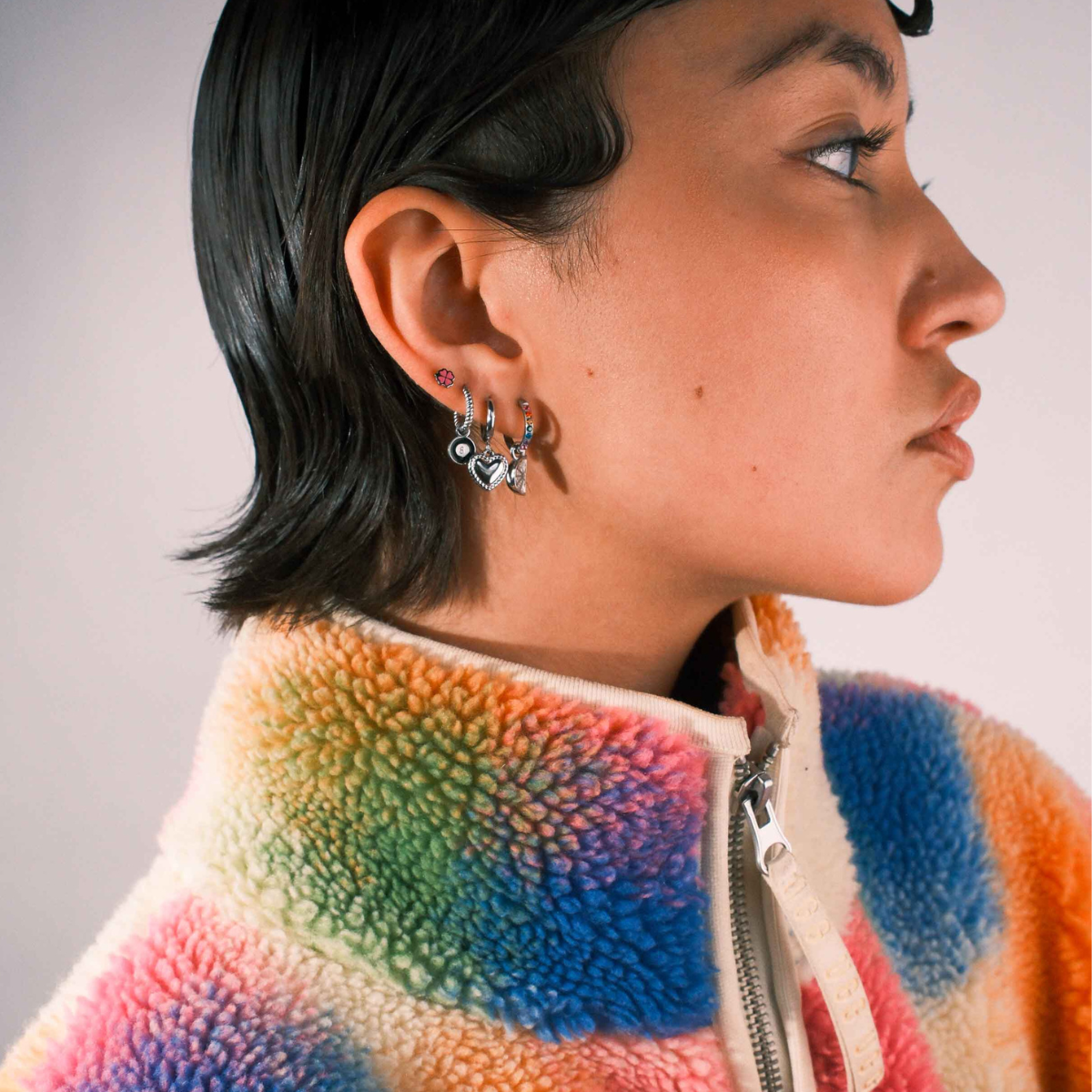 Close up of a model wearing multiple earrings against a blank background