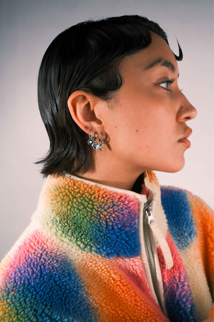Close up of a model wearing multiple earrings against a blank background
