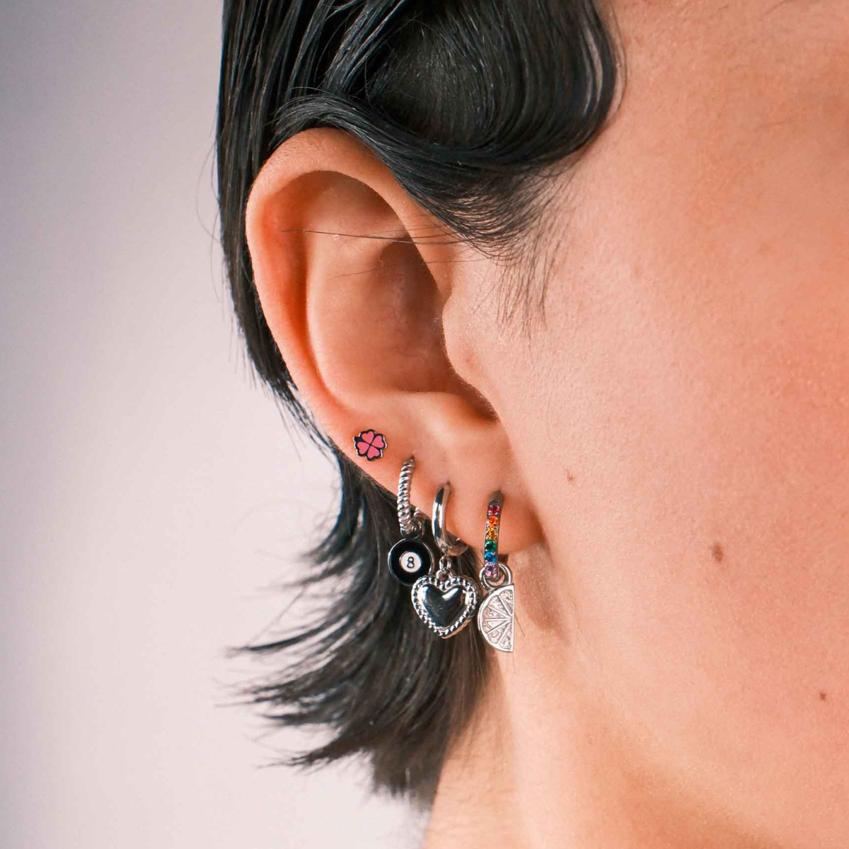 Close up of a model wearing multiple earrings against a blank background