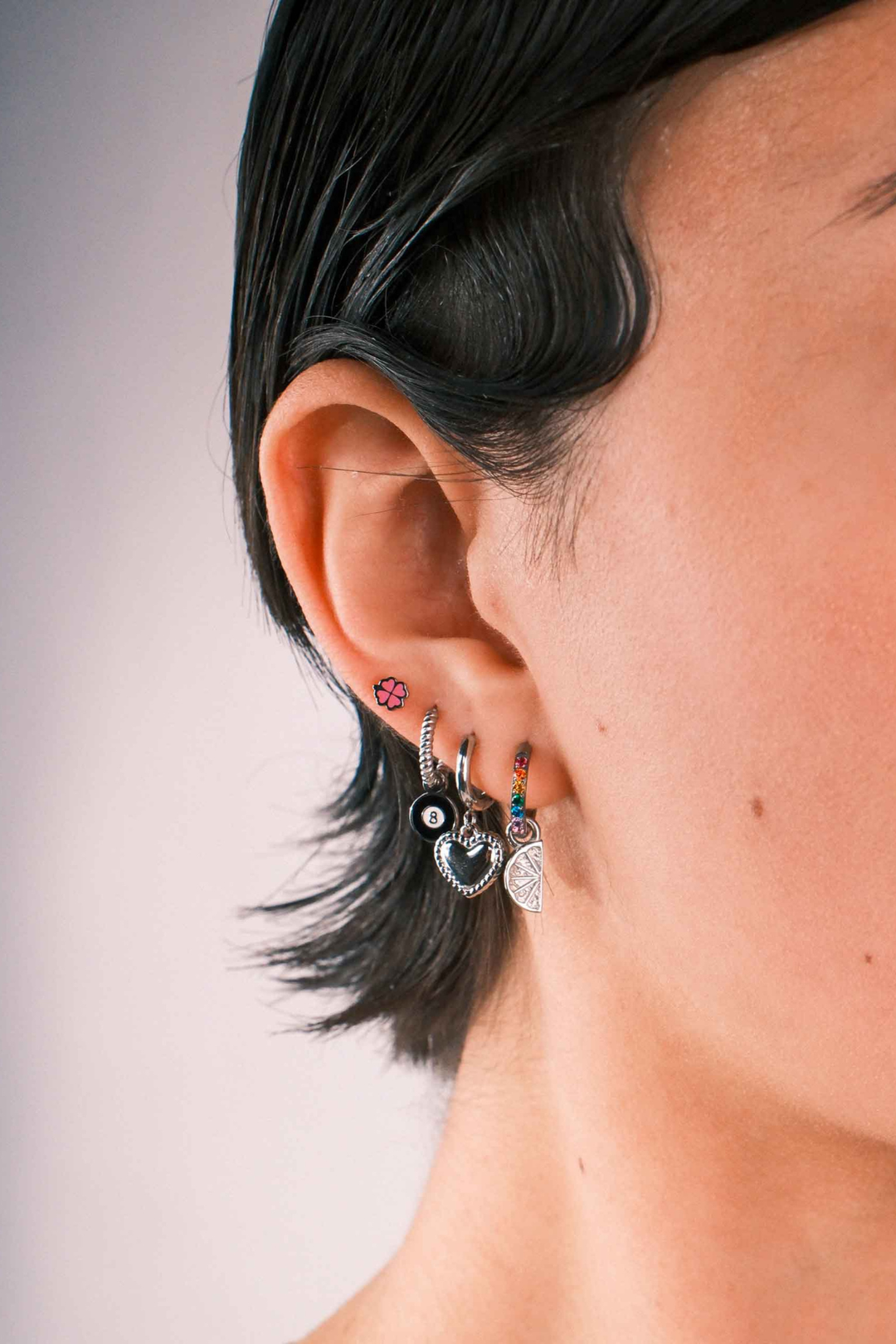 Close up of a model wearing multiple earrings against a blank background